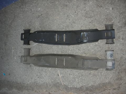 1990 Ford Mustang - Two car suspension control arms are shown side-by-side on a concrete surface.