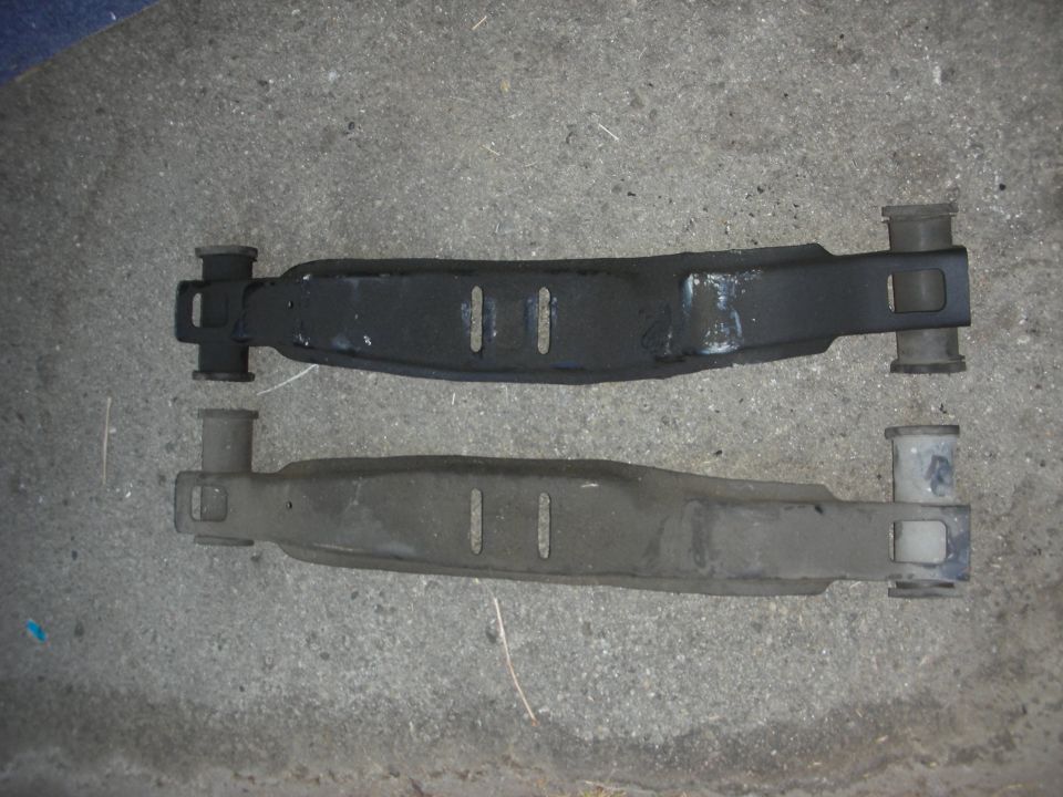 two car suspension control arms, one black and one gray, on concrete