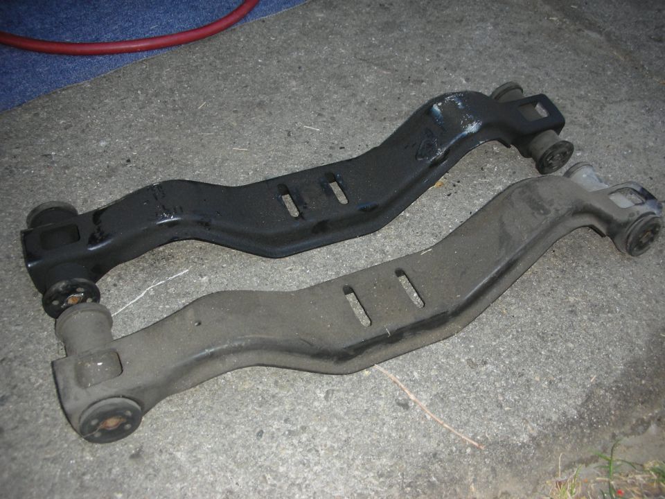 Two car control arms, one black and one gray, lying on concrete