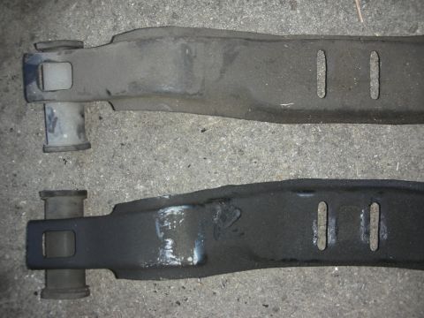 1990 Ford Mustang - Comparison of two automotive control arms, one appearing older and dustier than the other which has been cleaned or repainted.