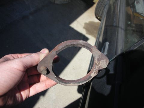 1990 Ford Mustang - Holding a rusty exhaust flange part. A car's window and tire are visible in the background.