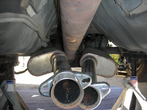 1990 Ford Mustang - Car's underbody showing dual exhaust pipes and driveshaft, raised on jack stands for maintenance.
