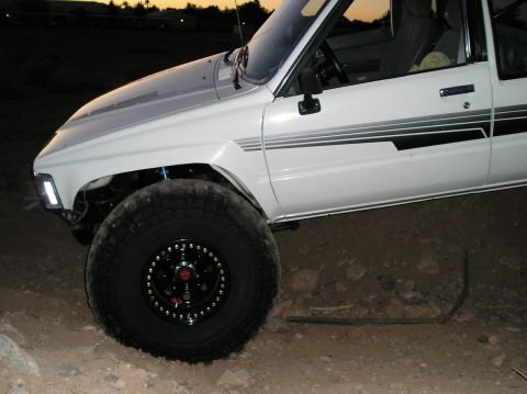 1986 Toyota Hilux - White pickup truck with aftermarket wheels and tires, seen from the front quarter angle at dusk.