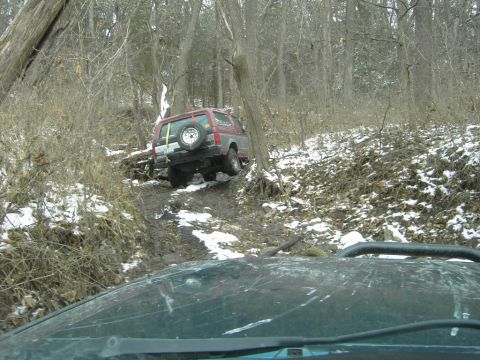 1995 Ford Bronco - An off-road vehicle navigates a challenging, muddy incline with patches of snow.