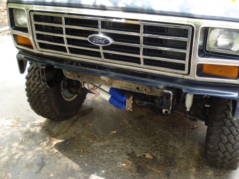 1984 Ford Bronco - The front grille and bumper of a 1984 Ford Bronco, showing aftermarket shocks and large tires.