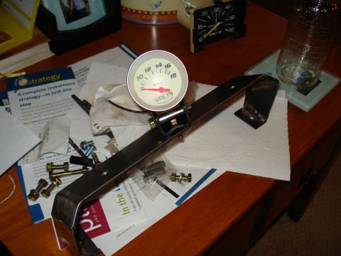 1984 Ford Bronco - A close-up view of a voltmeter gauge and its mounting hardware, surrounded by various documents and supplies.