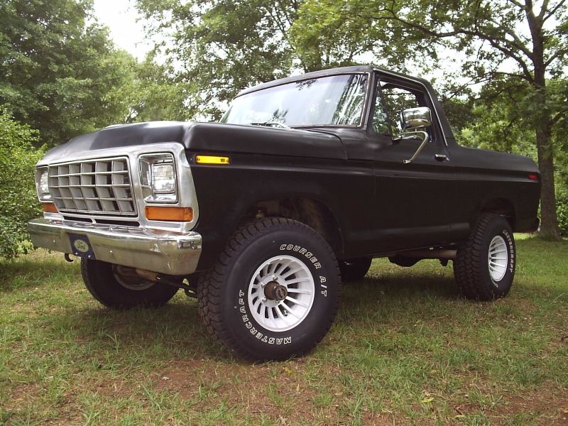 Flat-black early Ford Bronco SUV, front three-quarter view on grass
