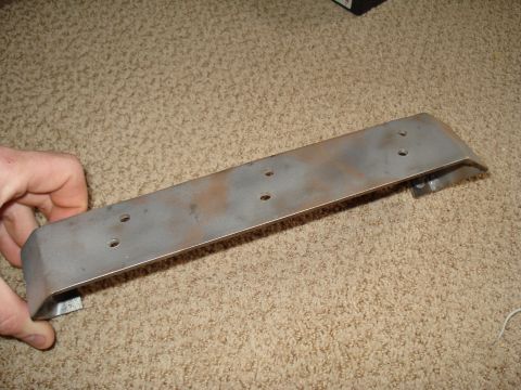 1984 Ford Bronco - A metal bracket with several mounting holes is shown, held by a hand against a carpeted surface.