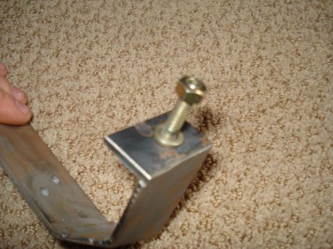 1984 Ford Bronco - A metal bracket with a bolt is shown against a carpeted background.