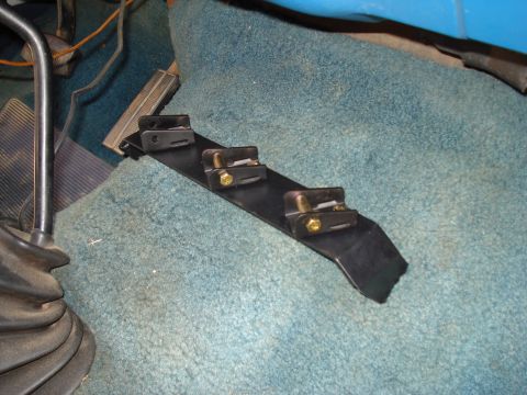 1984 Ford Bronco - A black metal bracket with three clamps is mounted on the blue carpeted floor of a vehicle's interior.