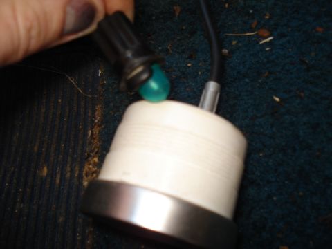1984 Ford Bronco - Close-up of the back of a small round gauge with a chrome bezel resting on blue vehicle carpet, while a hand holds the black bulb socket wi…