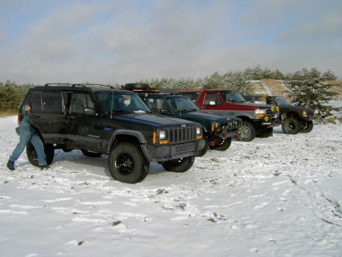 1995 Ford Bronco - Multiple off-road vehicles lined up in a snow-covered area under a cloudy sky.