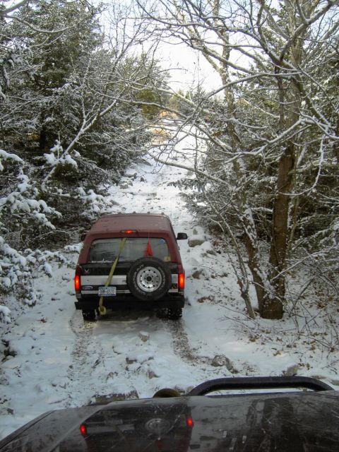 1995 Ford Bronco - A 1995 Ford Bronco navigates a challenging, snow-covered path through a wooded area.