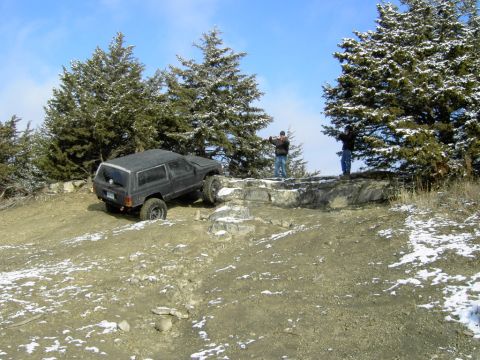 1995 Ford Bronco - A black SUV navigates a challenging rocky path in a snowy, wooded area with two onlookers.