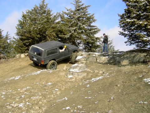1995 Ford Bronco - A black Jeep Cherokee XJ navigates a challenging rocky incline on a snowy day.
