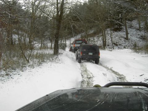 1995 Ford Bronco - Multiple SUVs navigate a snow-covered trail through a wooded area.