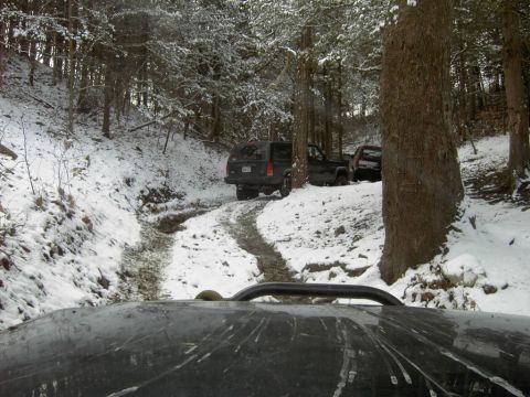 1995 Ford Bronco - Multiple Jeeps traverse a muddy, snow-covered forest trail. The view is from the perspective of one of the vehicles.