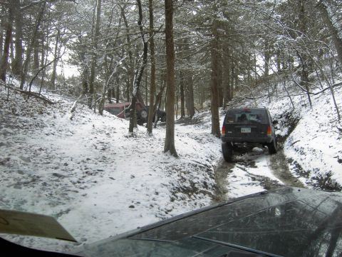 1995 Ford Bronco - Two vehicles navigate a challenging snowy trail through a wooded area.