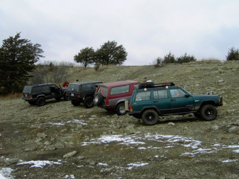 1995 Ford Bronco - Several SUVs, including a green Ford Bronco, are parked on a rocky, uneven terrain under an overcast sky.
