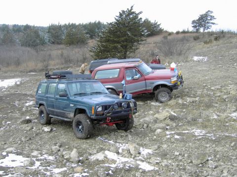 1995 Ford Bronco - A red and gray 1995 Ford Bronco is parked on a rocky, off-road trail alongside a blue Jeep.