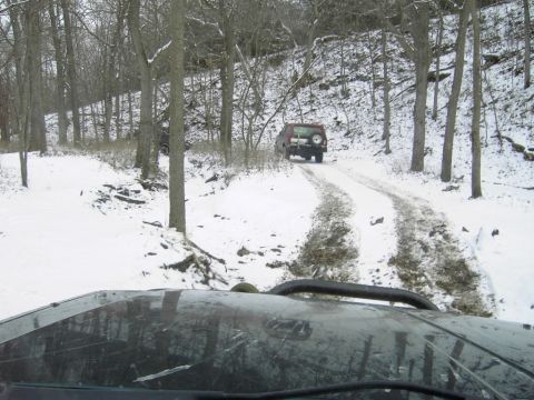 1995 Ford Bronco - Two SUVs navigate a snowy path in a wooded area during winter.