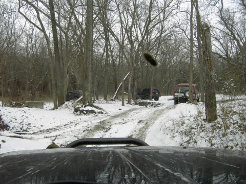 1995 Ford Bronco - Several SUVs navigate a snowy and muddy path through a forest during winter.