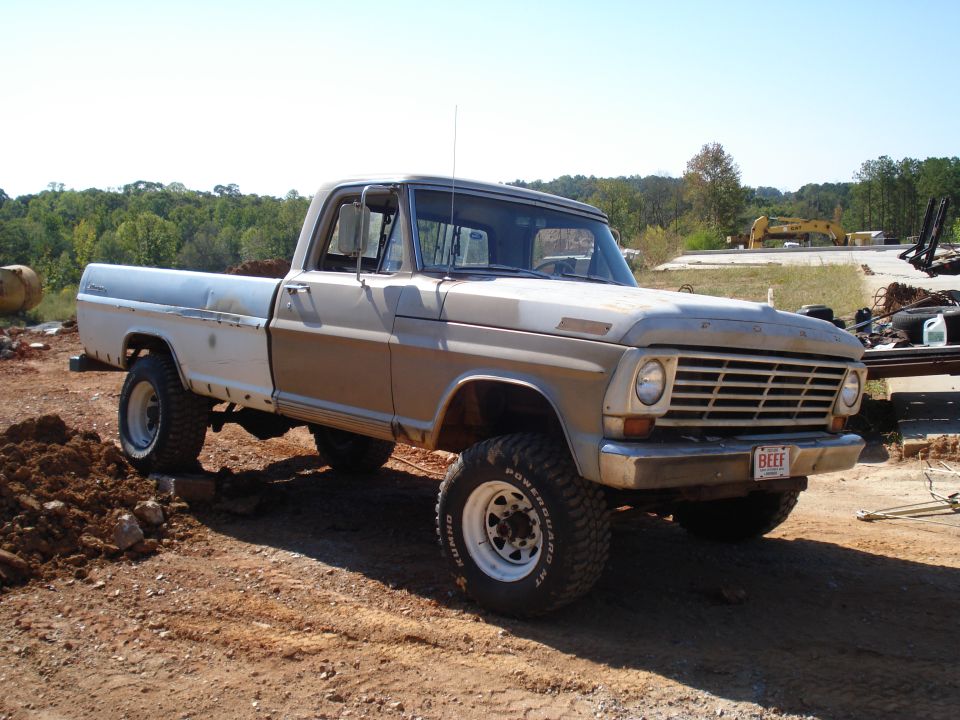 1967 Ford F-250 pickup truck with lifted suspension and off-road tires, parked on dirt. License plate reads 'BEEF'