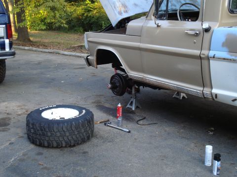 1967 Ford F-250 - Truck undergoing brake work with spare tire and tools laid out on the pavement.