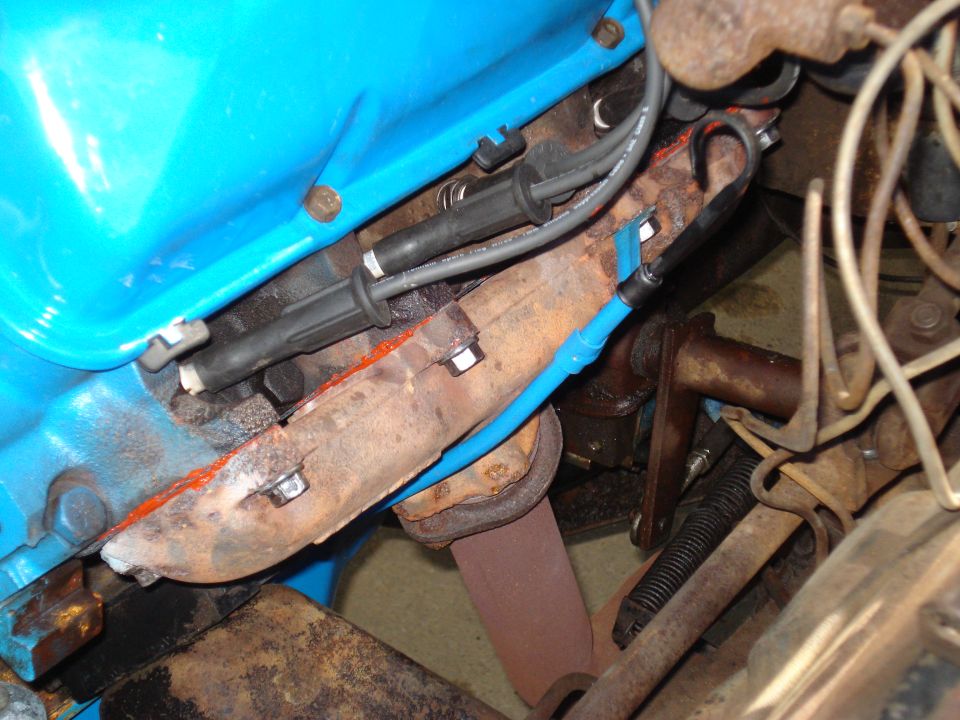Close-up of a rusty exhaust manifold with blue spark plug wires attached to a bright blue engine block