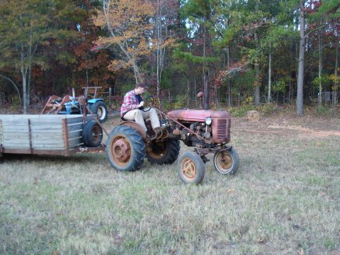 1967 Ford F-250 - A person drives a red tractor pulling a trailer through a grassy field with trees in the background.