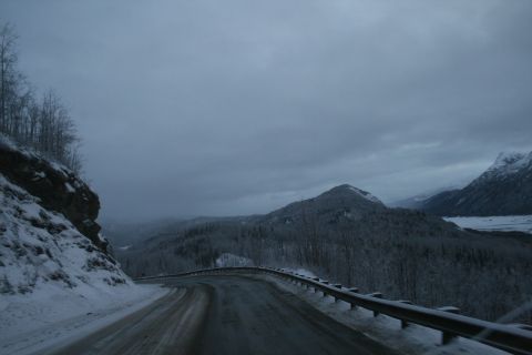 2003 Jeep TJ - A snowy mountain road winds through a forested landscape under a gray, overcast sky.