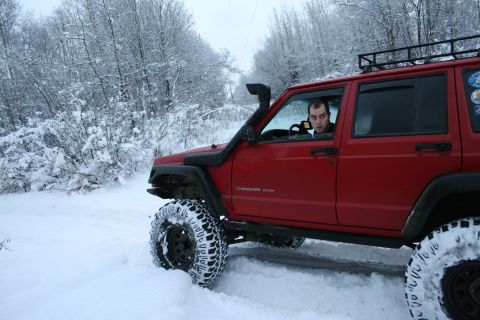 2003 Jeep TJ - A red Jeep Cherokee XJ navigates a snow-covered road, equipped with a snorkel and roof rack.