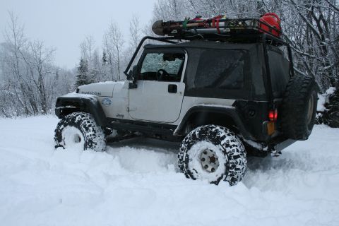 2003 Jeep TJ - A white Jeep Wrangler navigates through deep snow, equipped with a roof rack for outdoor gear.