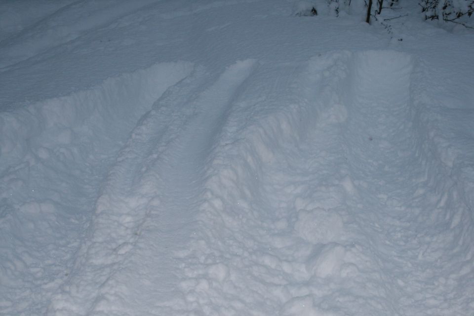 Tire tracks imprinted in deep snow, with some disturbed snowdrifts