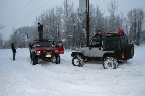 2003 Jeep TJ - Two Jeeps are stuck in the snow, with people standing around them in a winter scene.