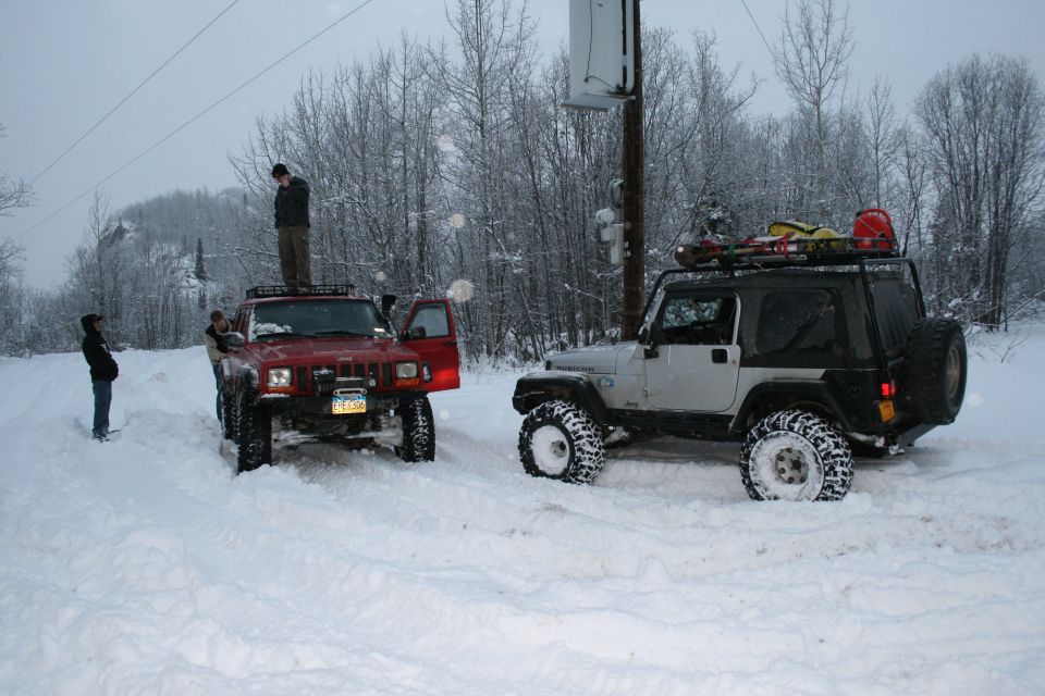 Two Jeeps, a red Cherokee and a silver TJ, stuck in deep snow. People stand around them