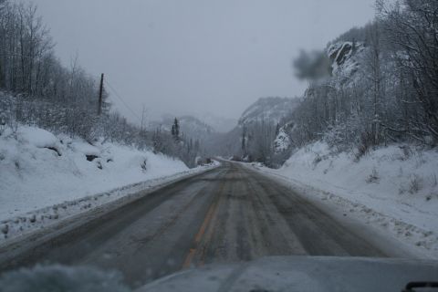 2003 Jeep TJ - Driving on a snow-covered mountain road with trees and rocky cliffs visible.
