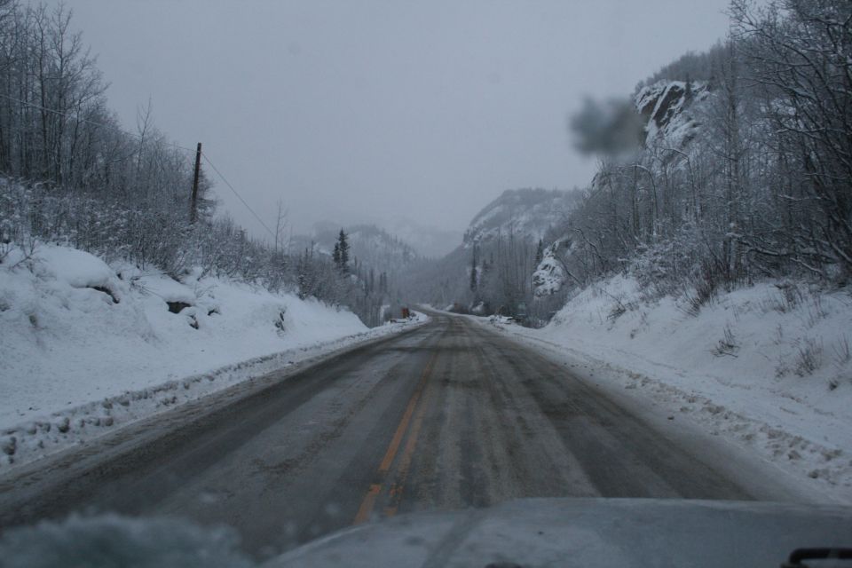 View from inside a vehicle driving on a wet, snowy road through a mountain pass