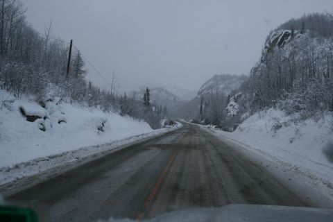 2003 Jeep TJ - A desolate, snow-covered road winds through a mountain landscape under an overcast sky.