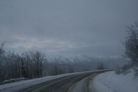 2003 Jeep TJ - A winding road covered in snow leads through a desolate winter scene with mountains in the distance.