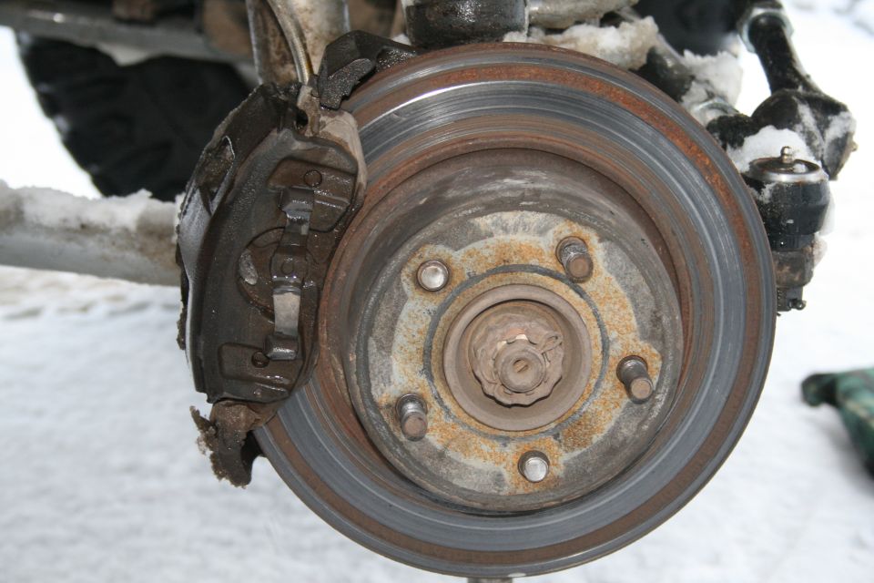 Close-up of a rusty Jeep TJ brake rotor and caliper with snow in the background