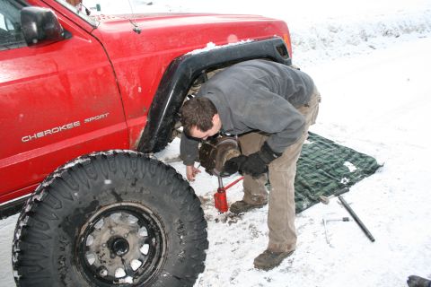2003 Jeep TJ - A person works on the brakes of a red Jeep Cherokee Sport in a snowy environment.