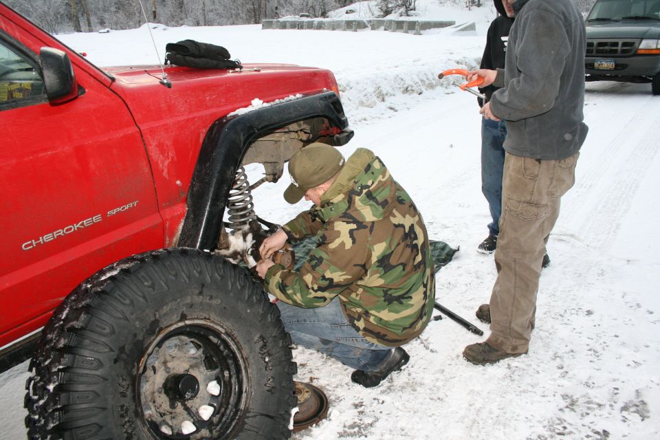 Red Jeep Cherokee Sport with "Cherokee Sport" visible, being worked on in the snow