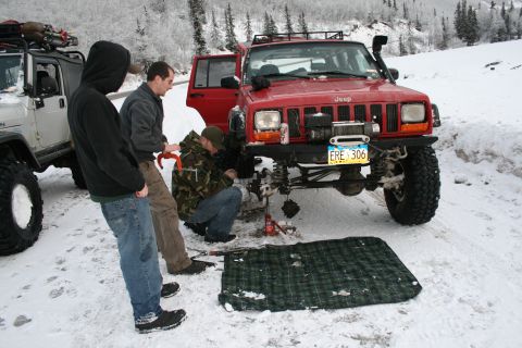 2003 Jeep TJ - People work on a red Jeep Cherokee XJ in a snowy environment next to a white Jeep Wrangler.