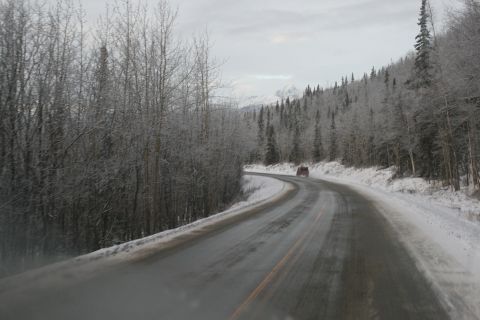 2003 Jeep TJ - A red SUV travels down a winding road in a winter landscape with snow on the trees and ground.