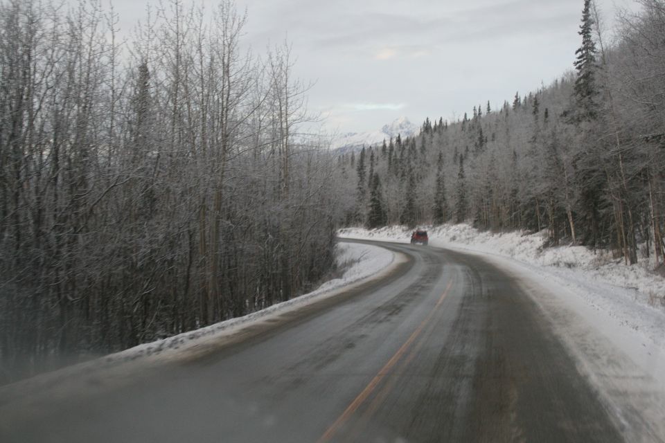 Red SUV drives on a wet, icy road through a snow-covered forest