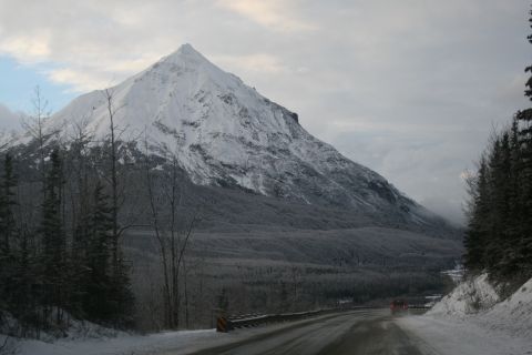 2003 Jeep TJ - A red vehicle travels down a snow-covered road, dwarfed by a massive, snow-capped mountain.