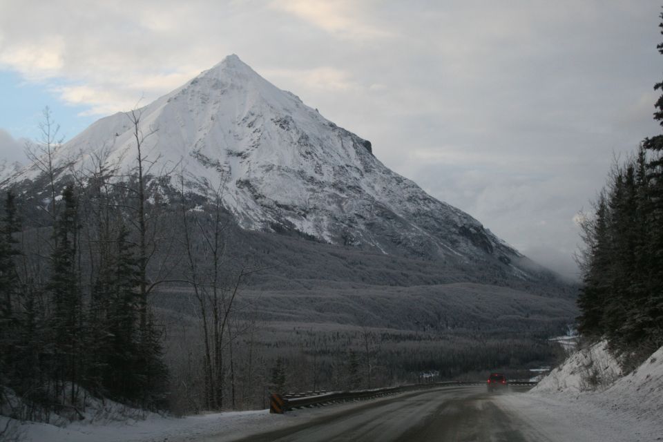Red vehicle driving on a wet, snowy road with a large snow-covered mountain in the background