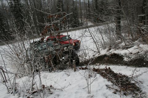 2003 Jeep TJ - A red and gray pickup truck is seen partially off-road in a snowy, wooded area.