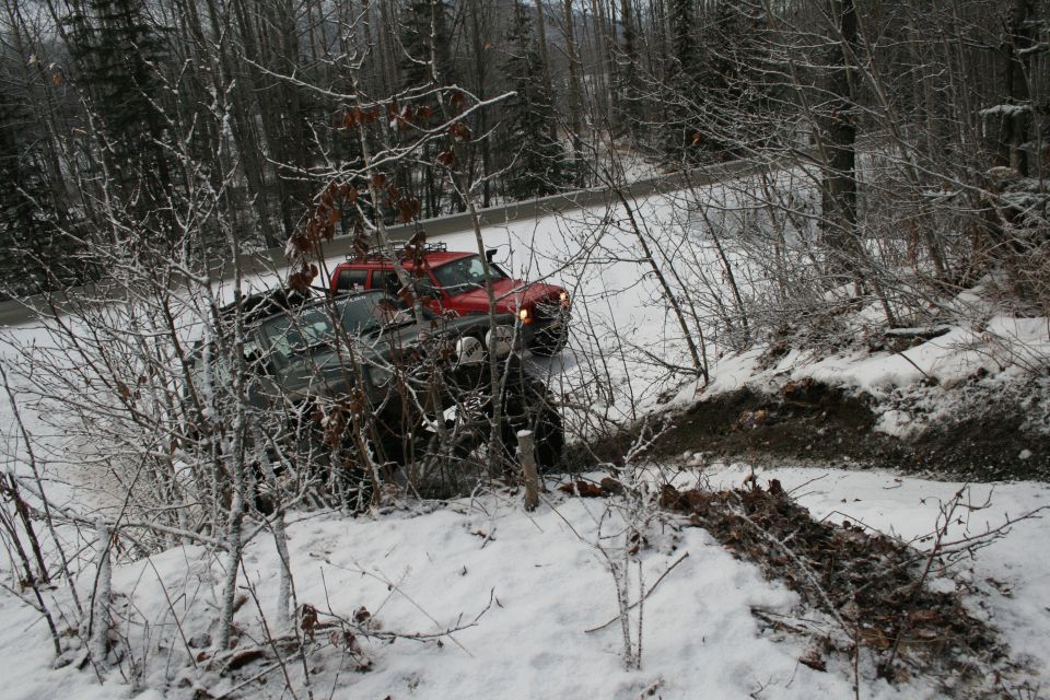 Red and gray pickup truck partially off-road in snow, with trees and brush